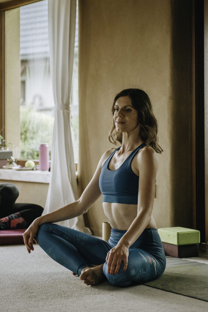 Trénerka jogy sedí v meditačnej pozícii počas hodiny jogy v interiéri.